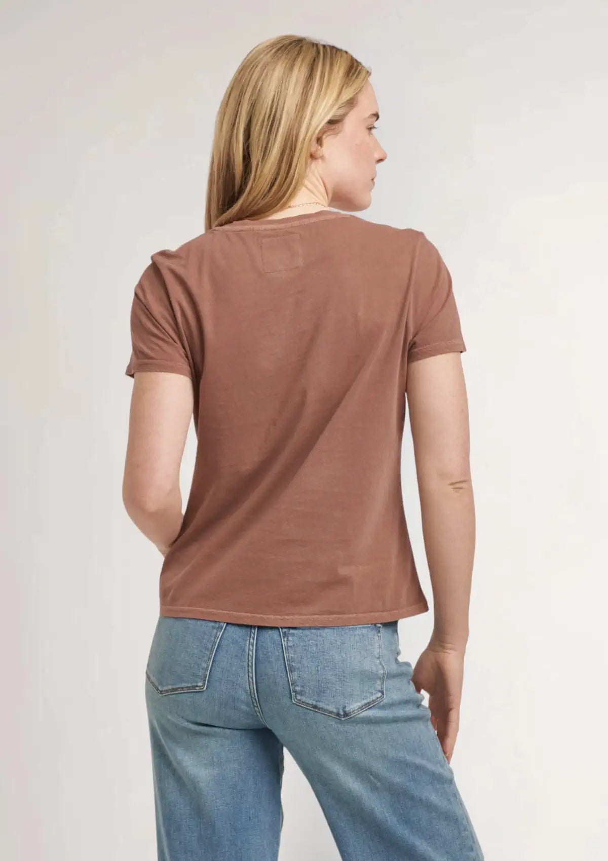 Brown tee paired with blue jeans and gold jewelry.
