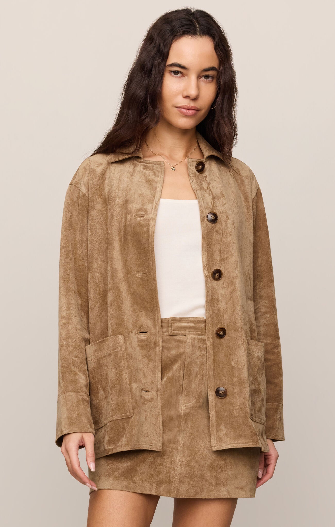 Woman wearing a brown suede jacket and skirt on a beige background